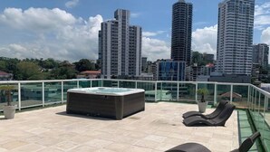 A rooftop terrace with a hot tub, lounge chairs, and a glass balustrade overlooking a cityscape with tall buildings. - 5B - Masterpiece! (Panamá)