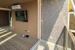 A modern hotel room with a wooden panel wall, a flat-screen TV mounted above a carpeted area, and a marble accent wall.
