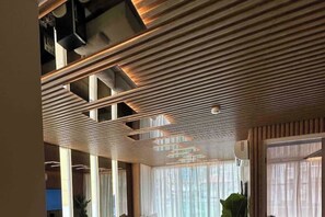 Un interior moderno con diseño de techo de listones, ventanas amplias con cortinas translúcidas y una unidad de aire acondicionado visible.
