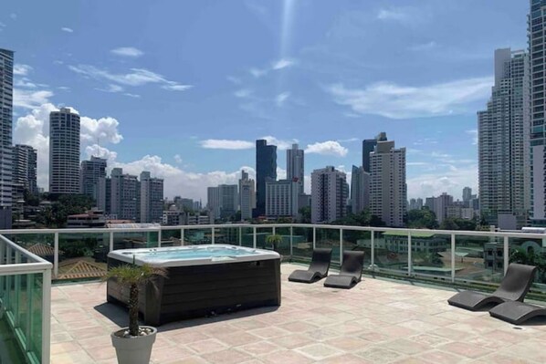 Terraza en la azotea con hidromasaje, sillones de descanso y vistas al horizonte de la ciudad.