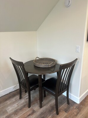 A dining area with a round table and four chairs, a woven placemat, and a light switch on the wall.