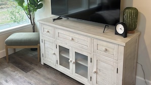 A flat-screen TV on a light wooden cabinet with drawers, a small green plant, and a cactus beside it.