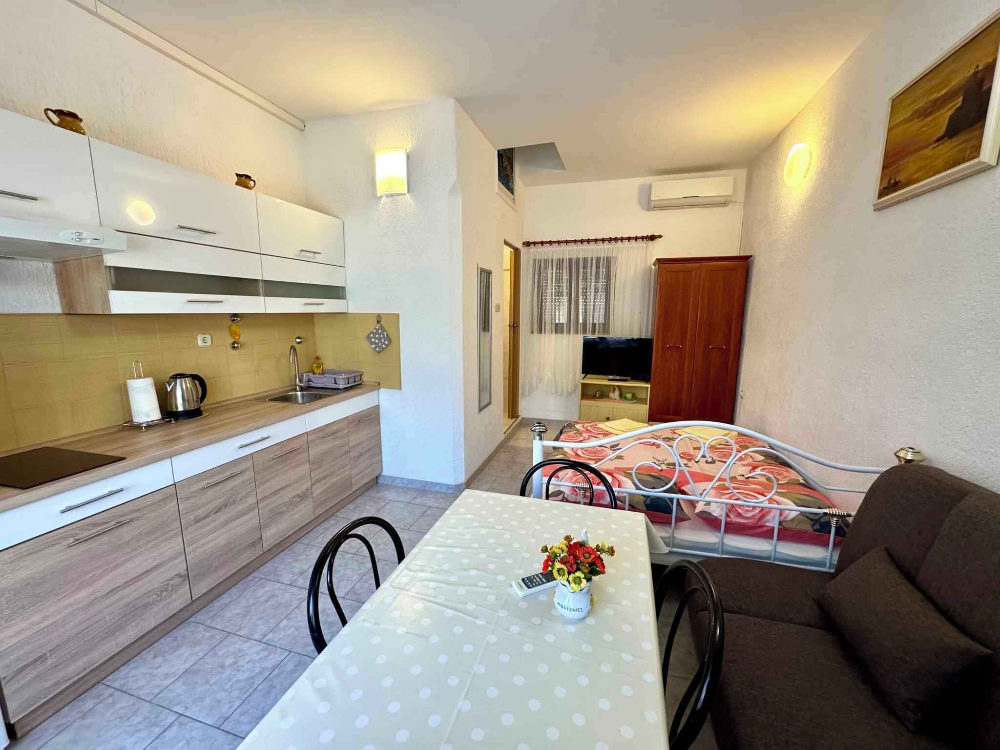 Un espacio habitable compacto con kitchenette, zona de comedor con mesa y sillas, sofá y televisor.