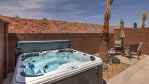 Un jacuzzi con panel de control, rodeado por un patio con sillas y una sombrilla, frente a un paisaje desértico.