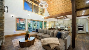 A spacious living area with a large sectional sofa, a wooden coffee table, and a view of the kitchen in the background. - Panorama Peak | 8BR Luxury Lodge w/ Pickleball, Game Room & Stunning Mountain Views (Broken Bow)