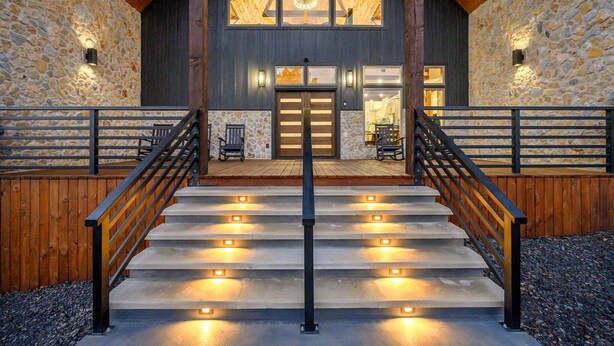 A grand staircase leading to a wooden door with a stone wall backdrop, flanked by two benches and a railing. - Panorama Peak | 8BR Luxury Lodge w/ Pickleball, Game Room & Stunning Mountain Views (Broken Bow)