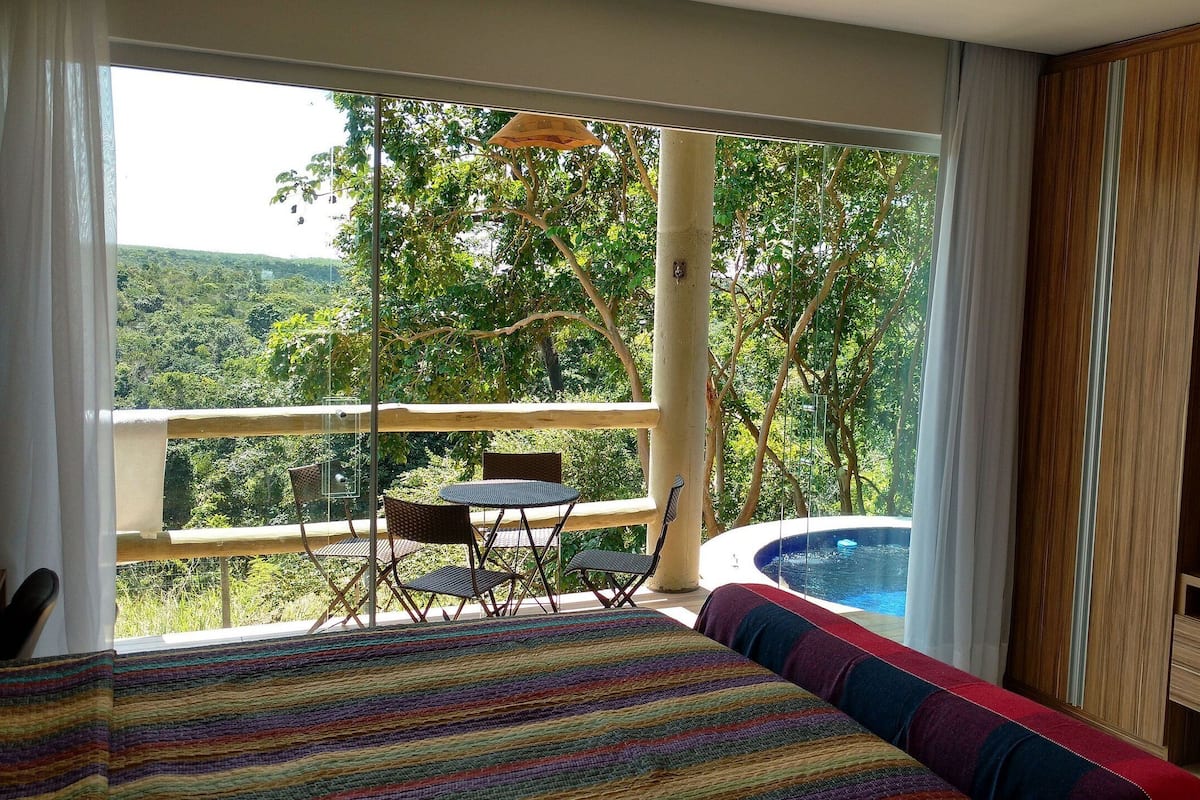 A bedroom with a large bed, a balcony with a table and chairs, and a hot tub.