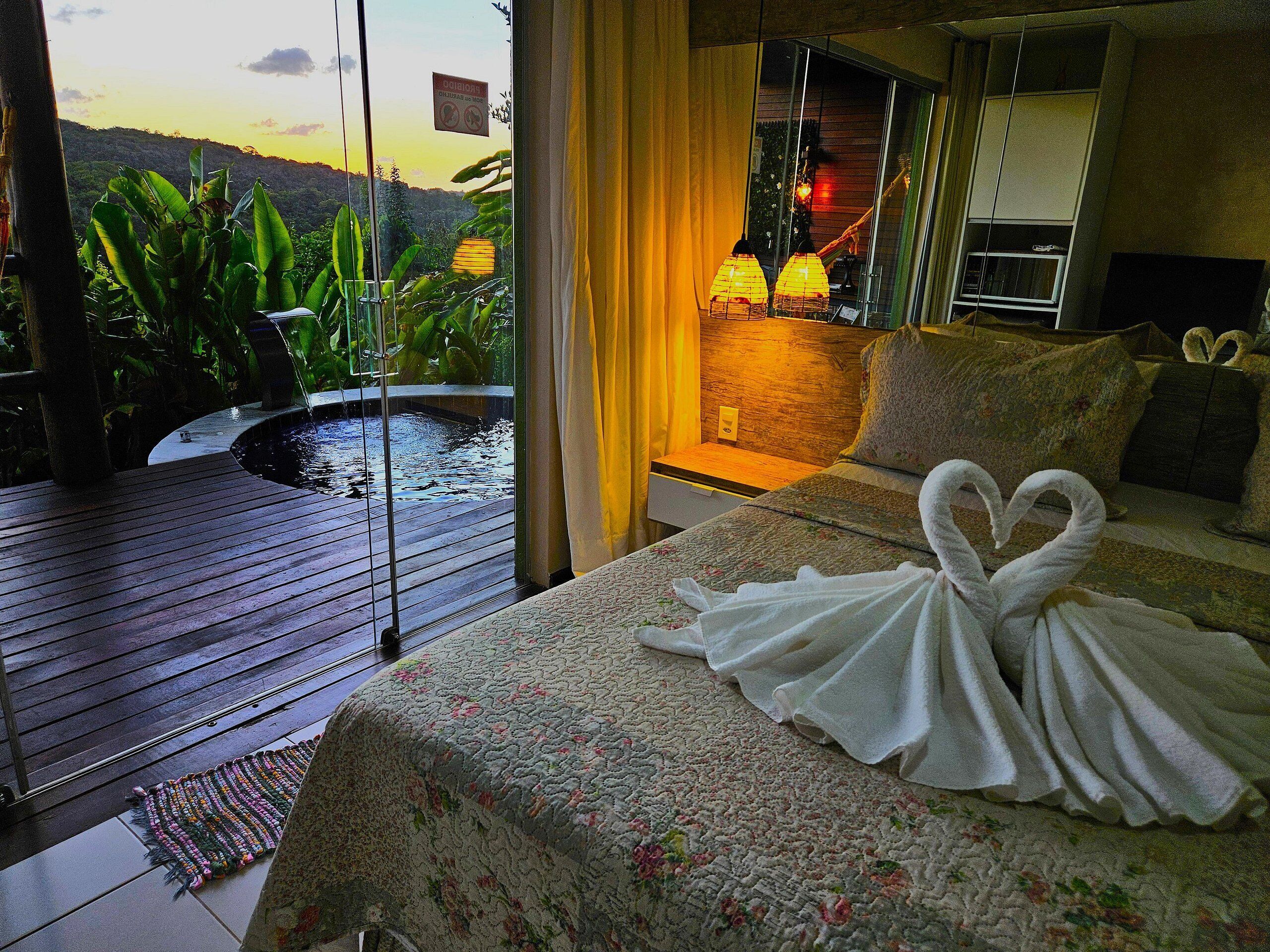 A bedroom with a bed, a window with a view of greenery, and a small pool.