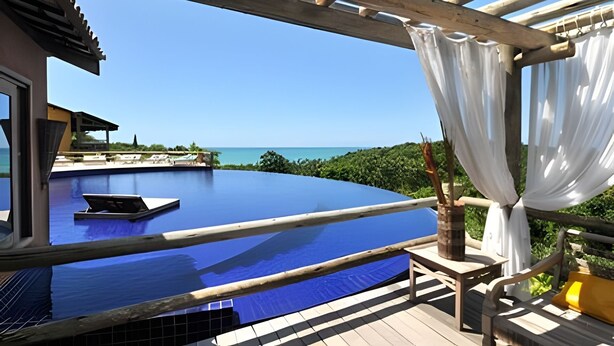 A rooftop infinity pool with a clear view of the ocean, wooden deck, and a pergola with white curtains. - Villas do Pratagy (Maceió)