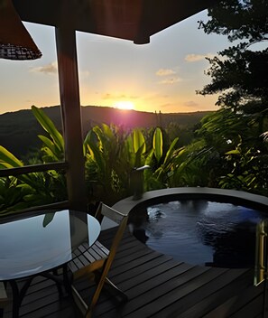 A hot tub on a wooden deck with a table and chairs, overlooking a lush landscape and a sunset. - Villas do Pratagy (Maceió)