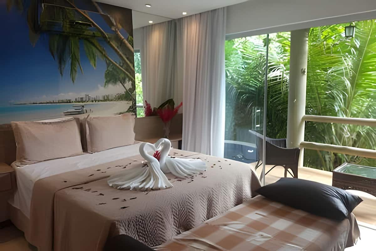 A hotel room with a bed, a sofa, a balcony with a view of greenery, and a painting of a beach scene.