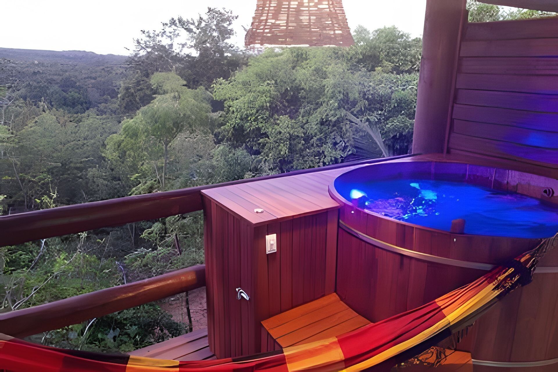 A wooden hot tub on a balcony with a view of a forested landscape.