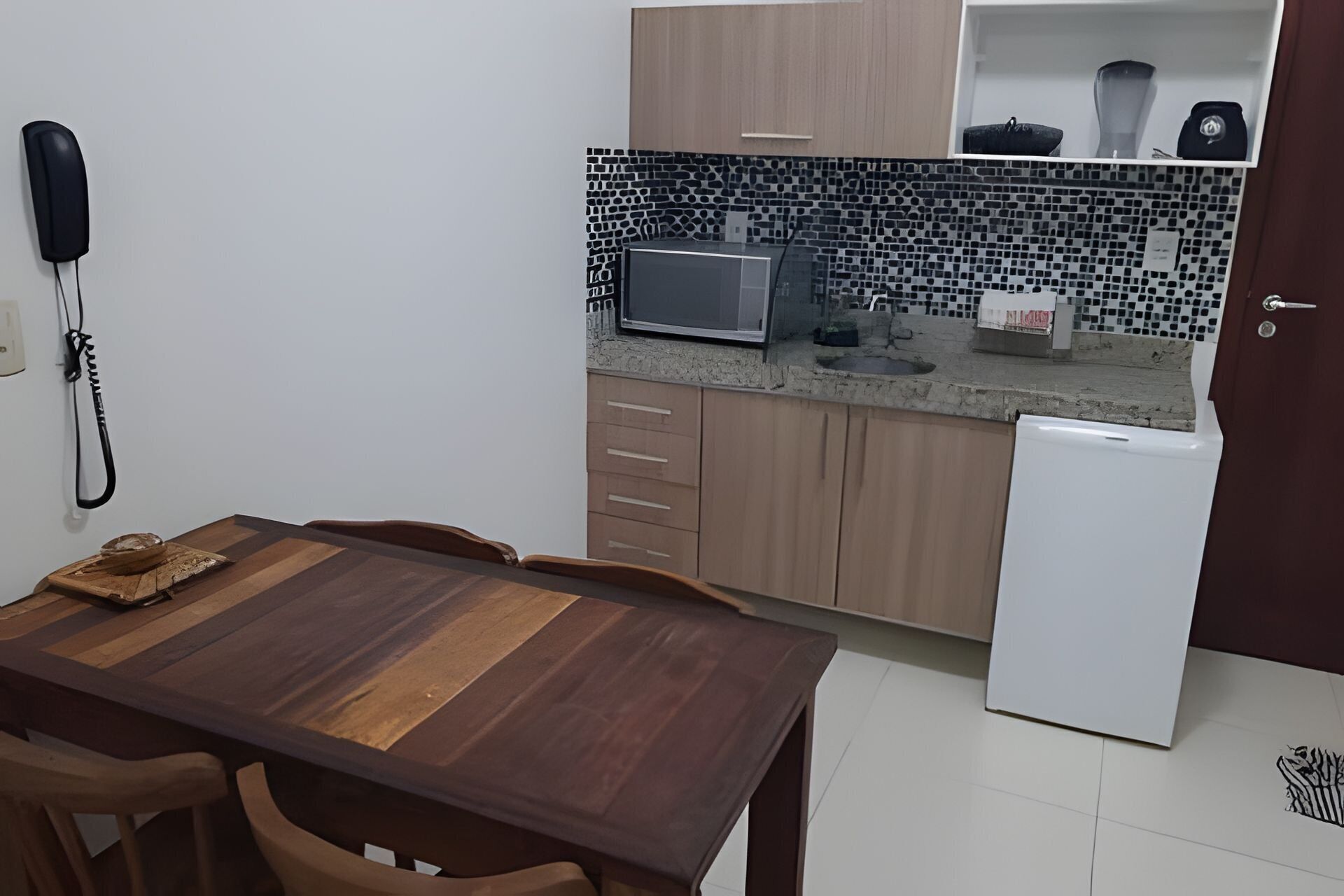 A compact kitchen with a microwave, a small refrigerator, and a tiled backsplash.