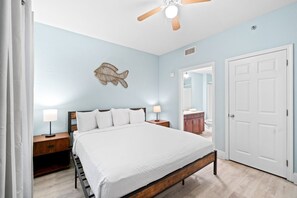 Un dormitorio con cama, mesitas de noche, ventilador de techo, un adorno de pez en la pared, una puerta y un espejo.