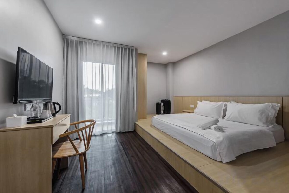Una habitación de hotel con una cama, un escritorio con silla, un televisor y una ventana con cortinas.