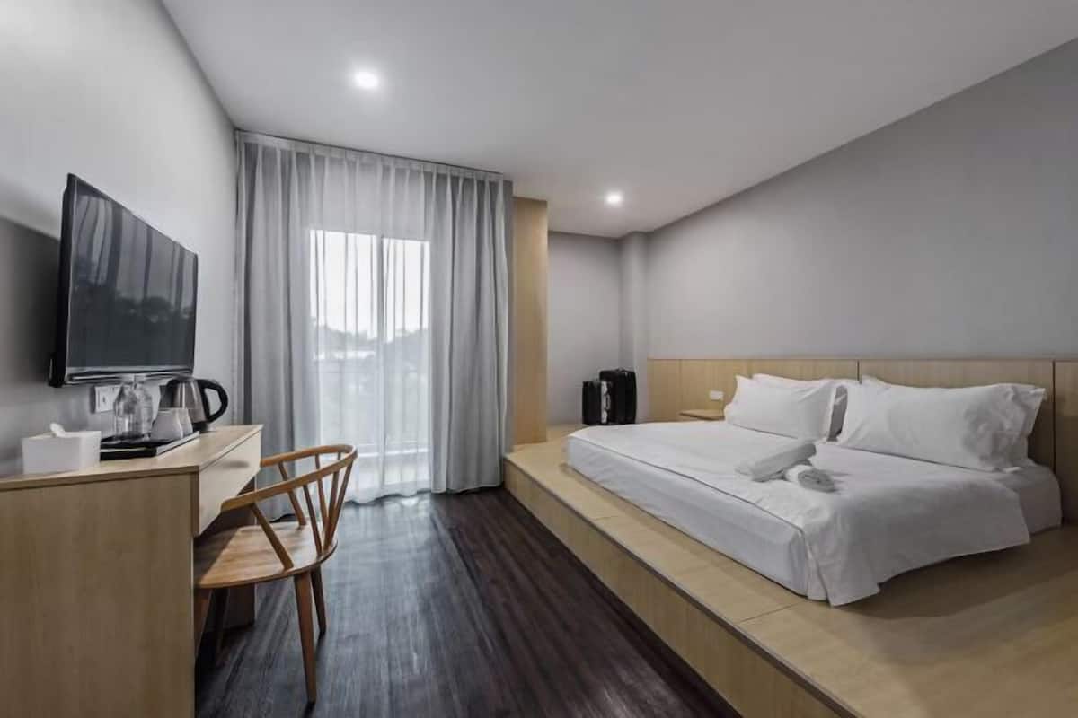 Een hotelkamer met een bed, een bureau met koffiezetapparaat, een stoel en een aan de muur bevestigde televisie.
