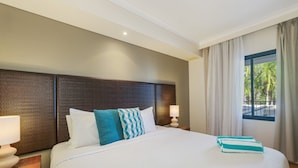 Une chambre d’hôtel avec un grand lit, deux tables de chevet avec des lampes, une tête de lit et une fenêtre avec des rideaux.