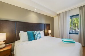 A hotel room with a large bed, two bedside tables with lamps, a headboard, and a window with curtains.