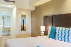 A hotel room with a bed, a nightstand with a lamp, a wall-mounted mirror, and a bathroom visible through an open door.