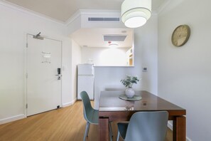 A modern kitchen with a refrigerator, a dining table with chairs, and a clock on the wall.
