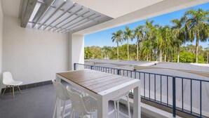 Un balcon avec une table et des chaises, une chaise blanche, et une vue sur des palmiers.