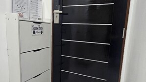 Puerta con un cartel que indica zona de guardado de zapatos, un armario blanco con cajones y una pared con carteles informativos.