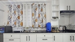 Una cocina con gabinetes blancos, encimera negra, un fregadero y un hervidor azul.