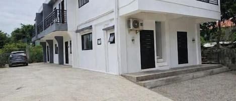 A two-story building with a balcony, a car parked in front, and a paved driveway.