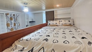 Un dormitorio con techo de madera, cama con ropa de cama estampada, una mesita de noche y una ventana con cortinas.
