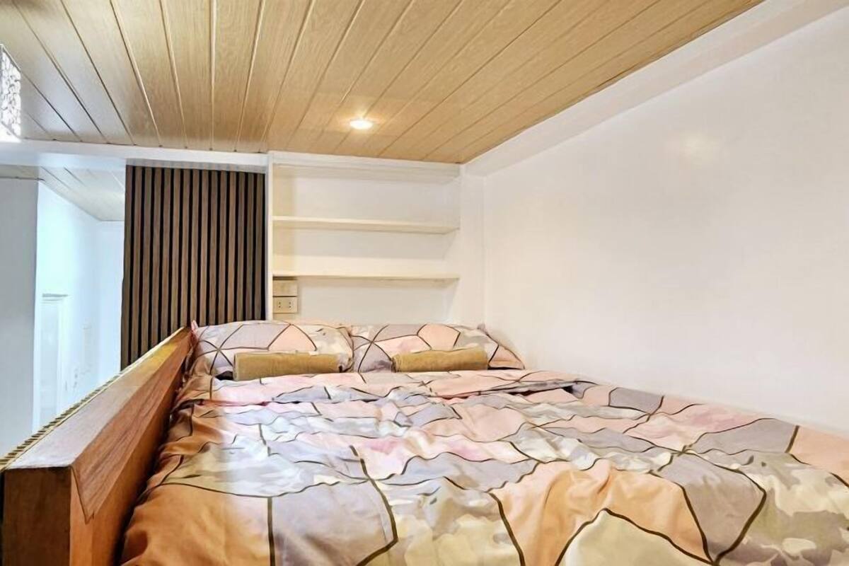 Une chambre avec un plafond en bois, un lit avec une literie à motifs et une bibliothèque intégrée.