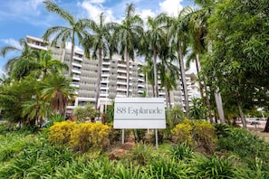 Señal que indica '88 Esplanade', con un edificio de varios pisos al fondo, rodeado de exuberante vegetación y palmeras.