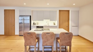 A modern kitchen with a central island, three bar stools, and a refrigerator.