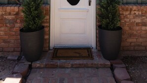 A white door with an oval window, flanked by two potted plants, and a black pendant light above. - Restored Vintage Carriage House in Mesa (Mesa)