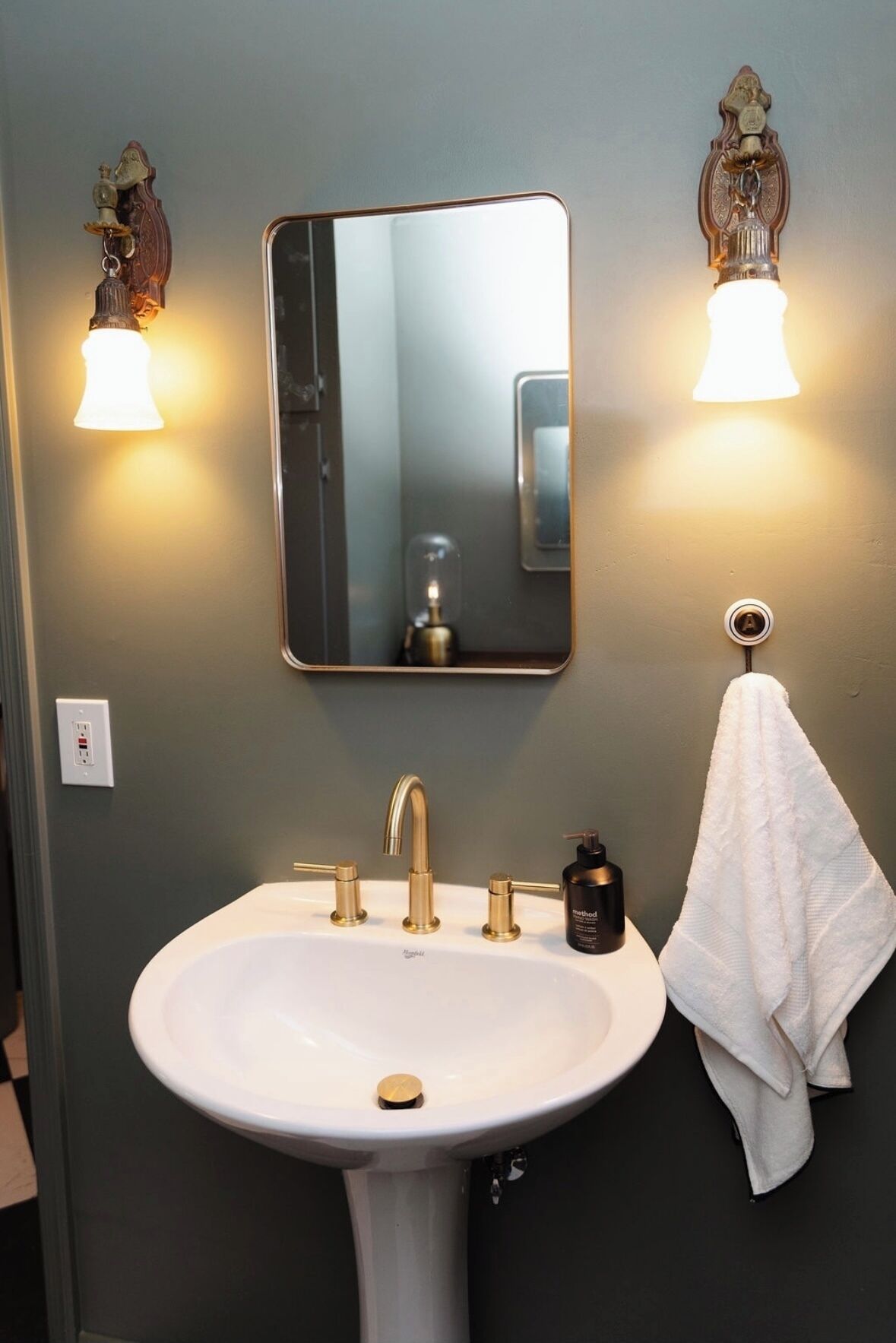 A bathroom with a white sink, gold faucets, a mirror, and two wall-mounted light fixtures.