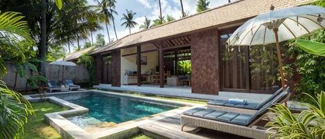 A poolside area with a lounge chair, a covered seating area, and a pool.