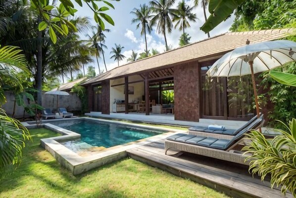 A poolside area with a lounge chair, a covered seating area, and a pool.
