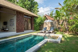 A swimming pool with lounge chairs, a stone wall, and lush greenery.