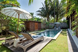 A pool area with lounge chairs, a wooden deck, and a small building with a wooden door.