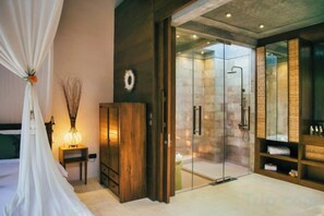 A bedroom with a bed, a nightstand, a wardrobe, a glass shower enclosure, and a vanity with a mirror. - Ruby Romance Oceanside Villa (Bali)
