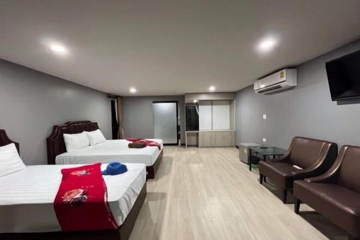 Ein Hotelzimmer mit zwei Betten, einer Sitzecke inklusive Sofa und Sesseln, einem kleinen Tisch und einem an der Wand montierten Fernseher.