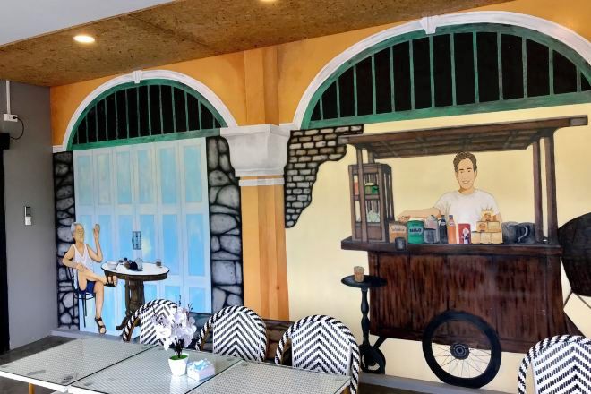 A restaurant with a mural of a street scene, a counter with a server, and a seating area with patterned chairs.