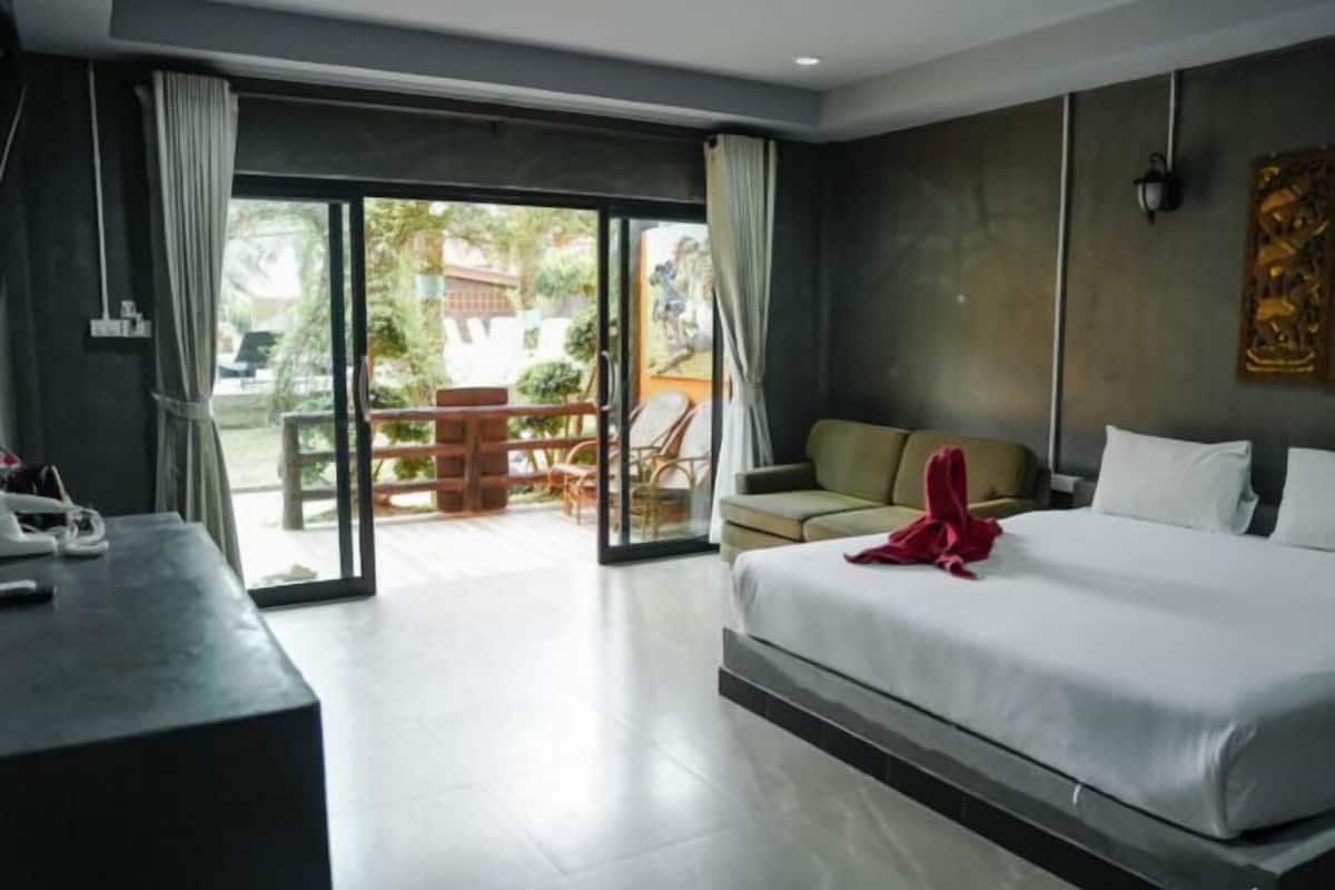 Ein Hotelzimmer mit einem Bett, einem Schreibtisch, einer Couch und einer Glasschiebetür, die zu einem Außenbereich mit Tisch und Stühlen führt.