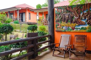 Une terrasse en bois avec deux chaises, une fresque représentant des animaux sauvages et un bâtiment aux toits rouges.