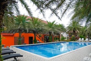 Una piscina circondata da palme e lettini, con un edificio sullo sfondo.