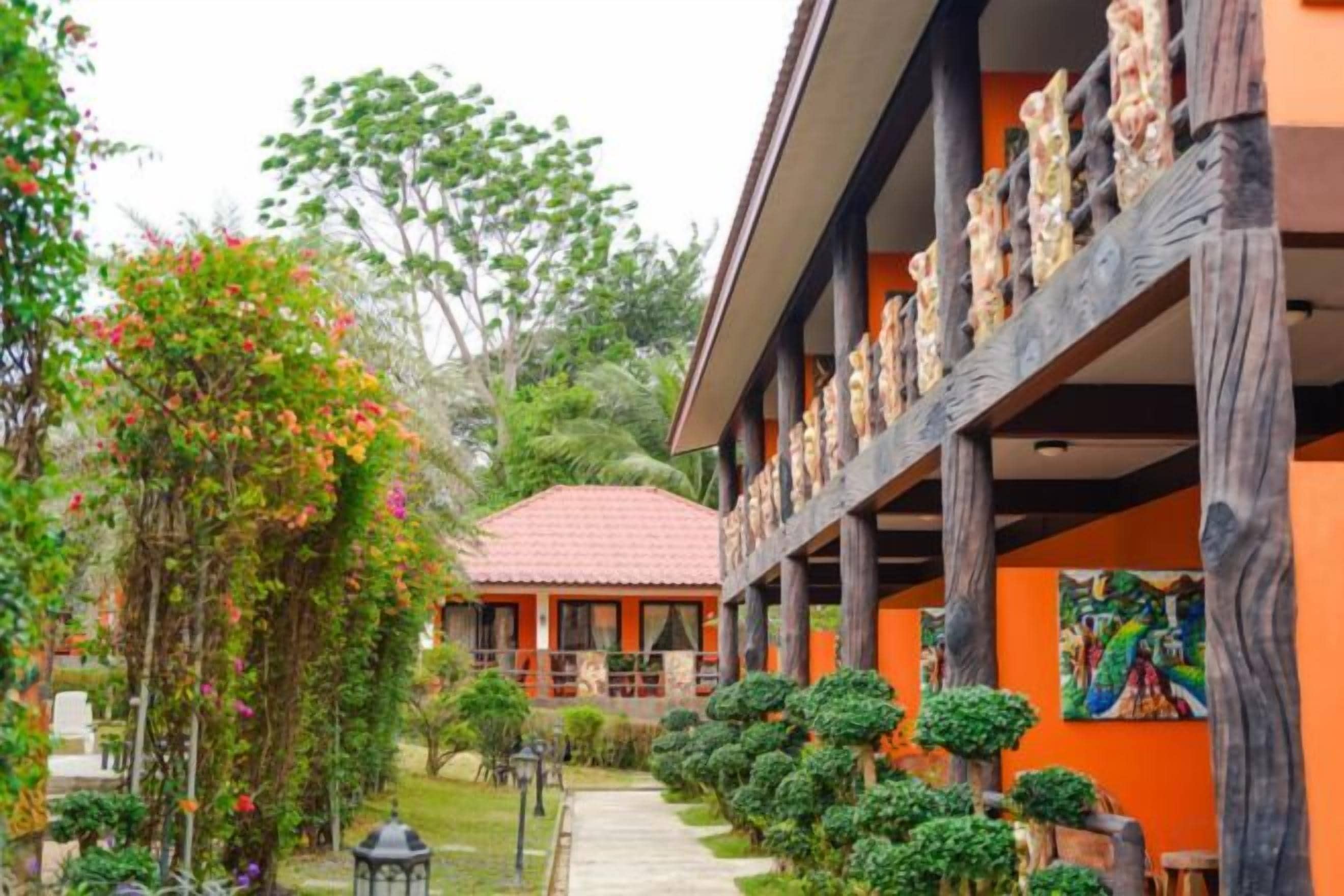 A building with a red-tiled roof, a covered walkway, and a garden with various plants and a pathway.