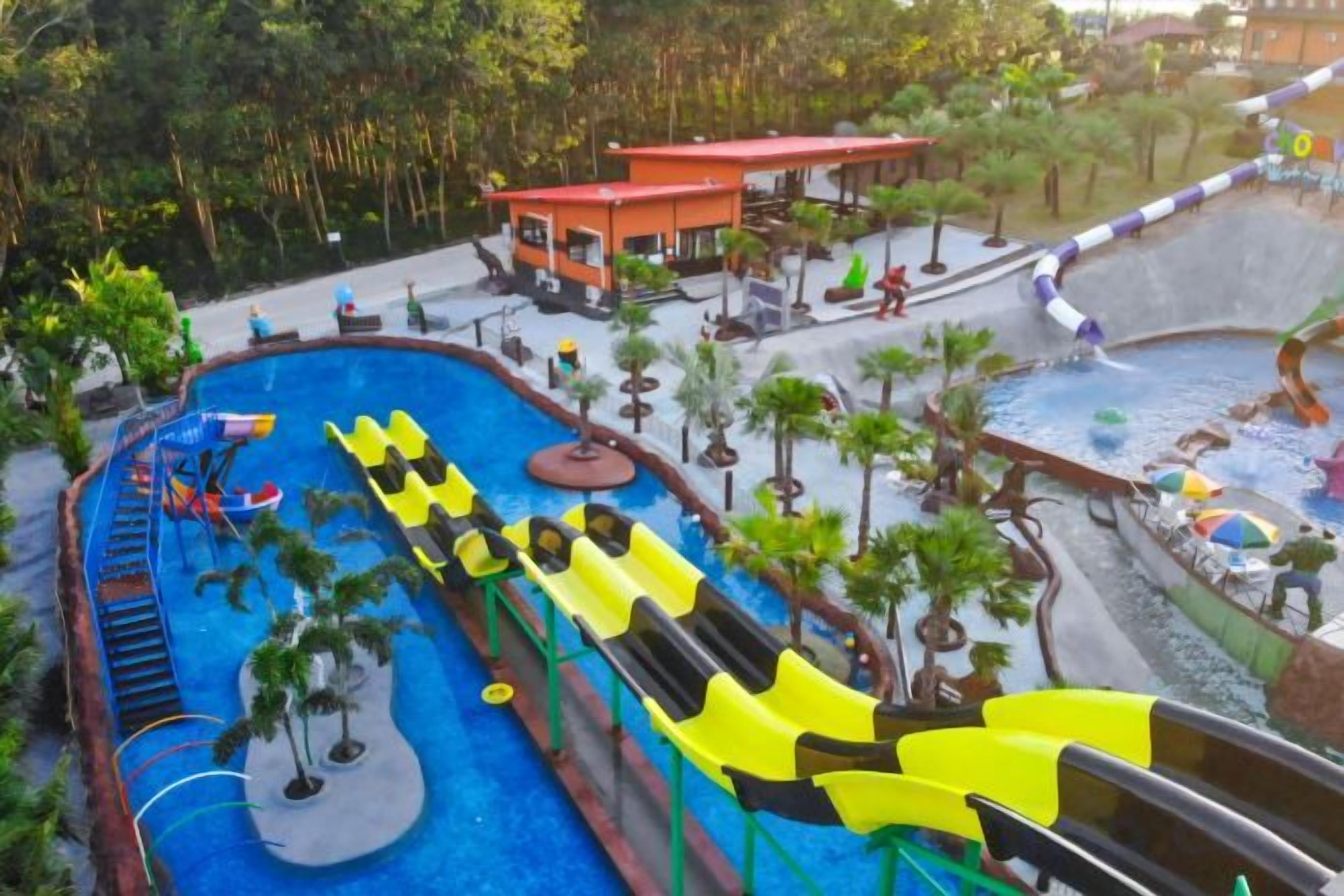 A water park with multiple slides and pools, surrounded by palm trees and a covered seating area.