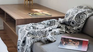 Een gezellige zithoek met een beklede bank, een decoratieve plaid en een tafeltje met een plant.