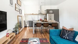 Een moderne woonkamer met een grote televisie, een blauwe bank en een eethoek, met een keuken op de achtergrond.