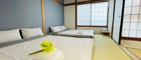 A traditional Japanese-style room with tatami flooring, two beds, and sliding doors.