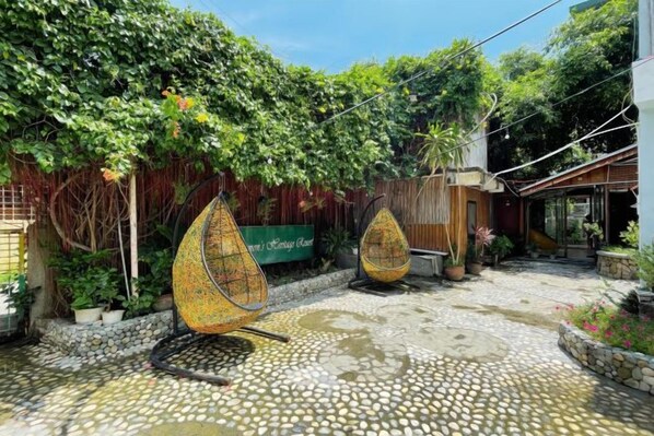 A courtyard with a stone floor, two hanging chairs, and a wooden fence. - Simons Heritage Resort Puerto Galera (Puerto Galera)